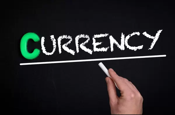 Hand schreibt das Wort "Currency" - Währung - mit Kreide auf eine schwarze Tafel