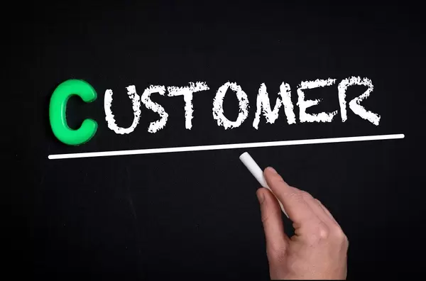 Hand schreibt das Wort "Customer" - Kunde - mit Kreide auf eine schwarze Tafel