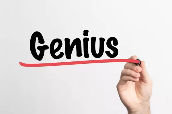Hand schreibt das Wort "Genie / Genialität" auf ein Whiteboard