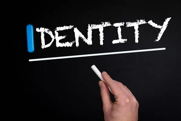 Hand schreibt das Wort "Identity" - Identität - mit Kreide auf eine schwarze Tafel