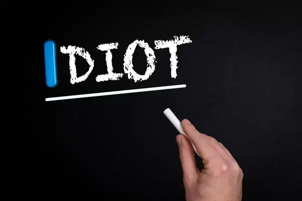 Hand schreibt das Wort "Idiot" mit Kreide auf eine schwarze Tafel