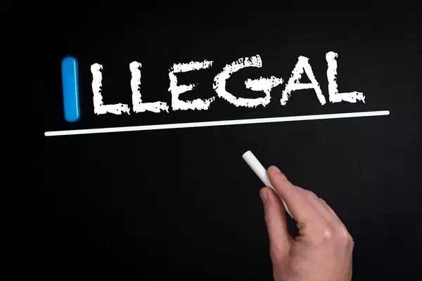 Hand schreibt das Wort "Illegal" mit Kreide auf eine schwarze Tafel
