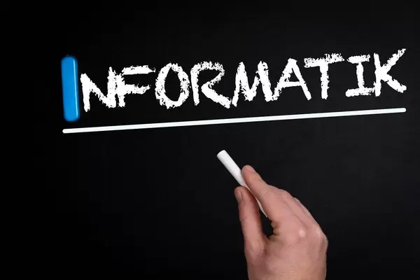 Hand schreibt das Wort "Informatik" mit Kreide auf eine schwarze Tafel