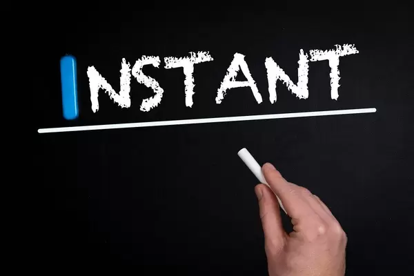 Hand schreibt das Wort "Instant" - sofort - mit Kreide auf eine schwarze Tafel