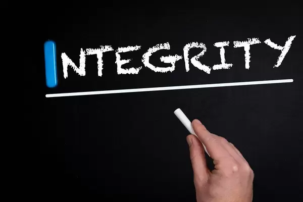 Hand schreibt das Wort "Integrity" - Integrität - mit Kreide auf eine schwarze Tafel