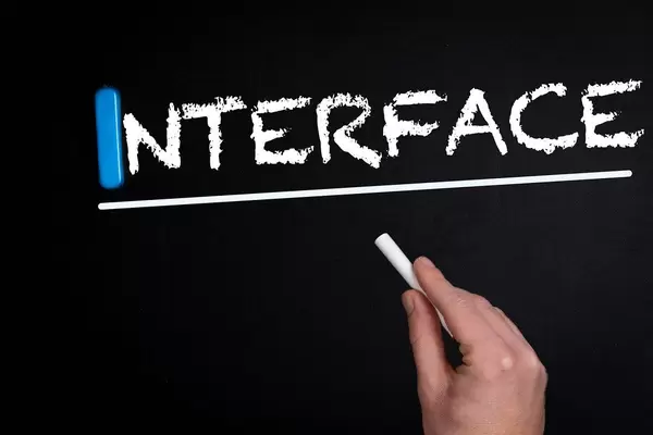 Hand schreibt das Wort "Interface" - Schnittstelle - mit Kreide auf eine schwarze Tafel