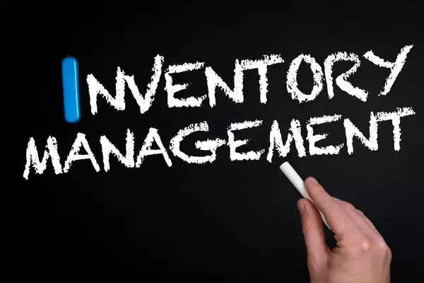 Hand schreibt das Wort "Inventory Management" - Bestandsmanagement - mit Kreide auf eine schwarze Tafel