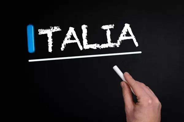 Hand schreibt das Wort "Italia" mit Kreide auf eine schwarze Tafel