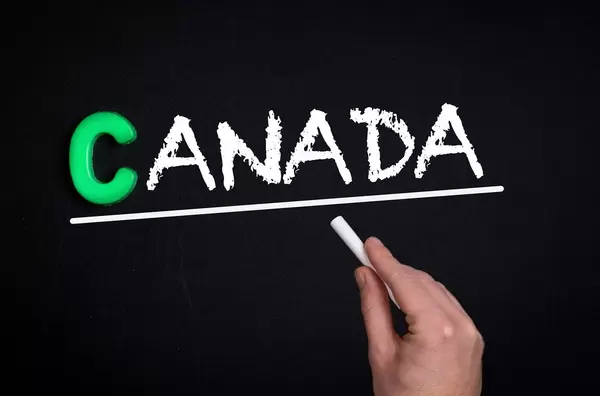 Hand schreibt das Wort "Kanada" mit Kreide auf eine schwarze Tafel