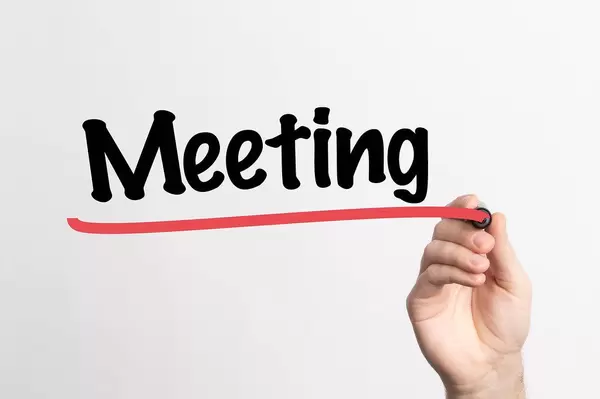 Hand schreibt das Wort "Meeting / Treffen" auf ein Whiteboard