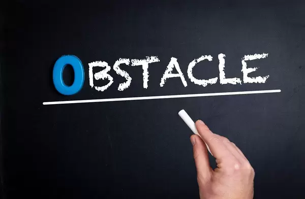 Hand schreibt das Wort "Obstacle" - Hindernis / Hürde - mit Kreide auf eine schwarze Tafel