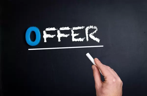 Hand schreibt das Wort "Offer" - Angebot - mit Kreide auf eine schwarze Tafel