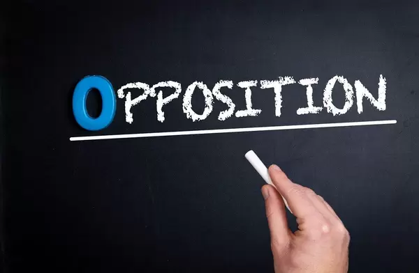 Hand schreibt das Wort "Opposition" - Gegenseite - mit Kreide auf eine schwarze Tafel