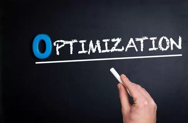Hand schreibt das Wort "Optimization" - Optimierung - mit Kreide auf eine schwarze Tafel