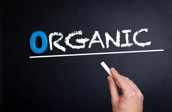 Hand schreibt das Wort "Organic" - biologisch - mit Kreide auf eine schwarze Tafel