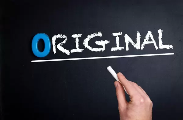 Hand schreibt das Wort "Original" mit Kreide auf eine schwarze Tafel