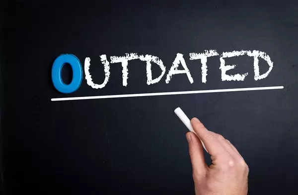 Hand schreibt das Wort "Outdated" - Veraltet - mit Kreide auf eine schwarze Tafel