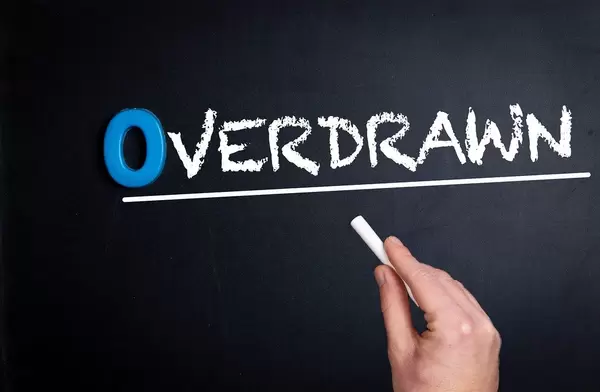Hand schreibt das Wort "Overdrawn" - überzogen / überzeichnet - mit Kreide auf eine schwarze Tafel