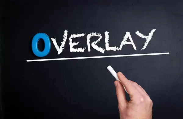 Hand schreibt das Wort "Overlay" mit Kreide auf eine schwarze Tafel
