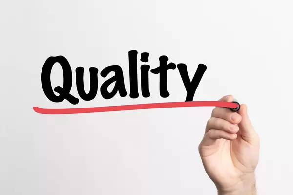 Hand schreibt das Wort "Qualität" auf ein Whiteboard