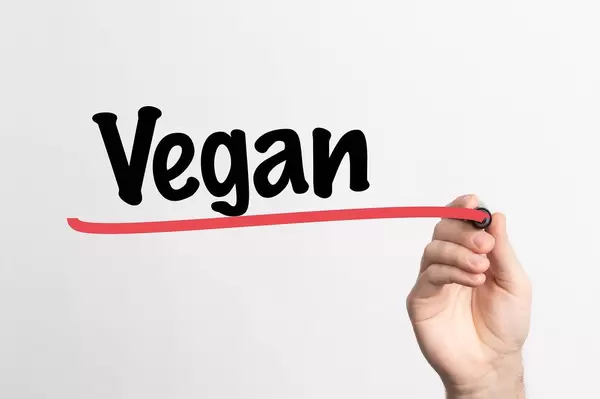 Hand schreibt das Wort "vegan" auf ein Whiteboard