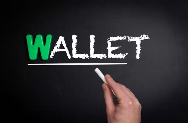 Hand schreibt das Wort "Wallet" - Geldbörse / Portemonnaie - mit Kreide auf eine schwarze Tafel