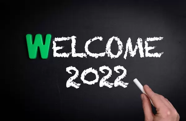 Hand schreibt das Wort "Welcome 2022" - Willkommen 2022 - mit Kreide auf eine schwarze Tafel
