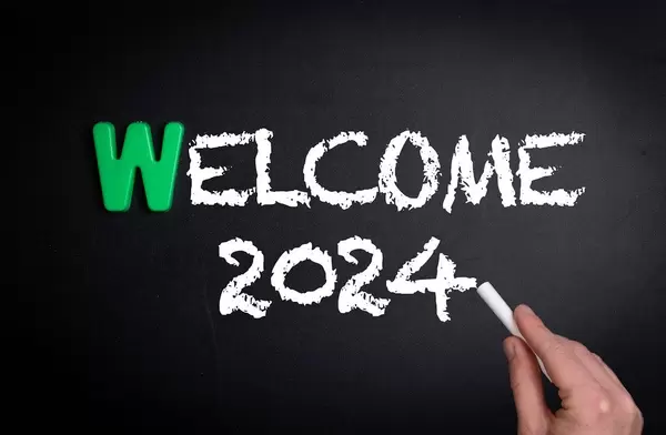 Hand schreibt das Wort "Welcome 2024" - Willkommen 2024 - mit Kreide auf eine schwarze Tafel
