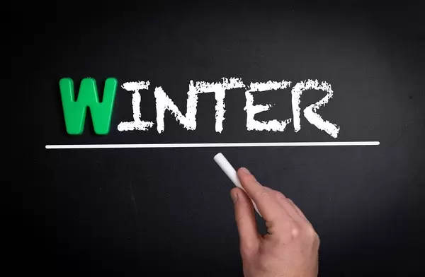 Hand schreibt das Wort "Winter" mit Kreide auf eine schwarze Tafel