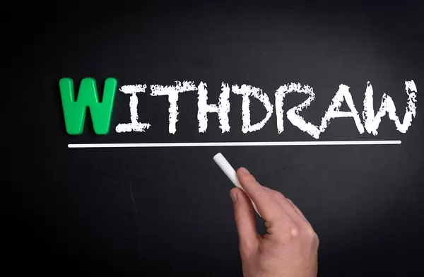 Hand schreibt das Wort "Withdraw" - zurücktreten - mit Kreide auf eine schwarze Tafel