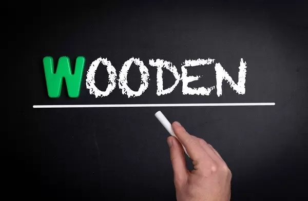 Hand schreibt das Wort "Wooden" - hölzern - mit Kreide auf eine schwarze Tafel