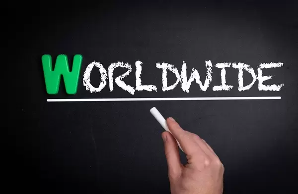 Hand schreibt das Wort "Worldwide" - weltweit - mit Kreide auf eine schwarze Tafel