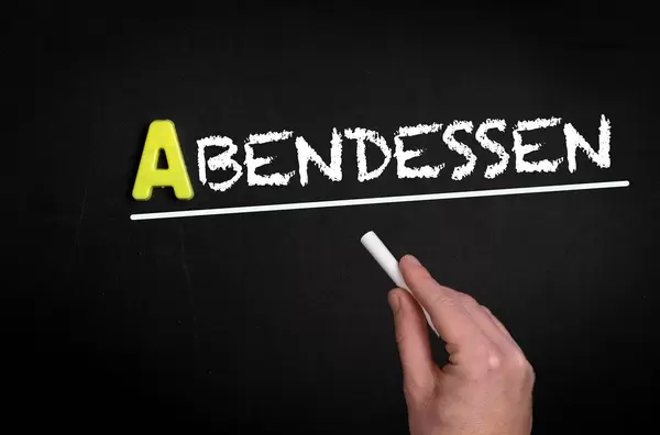 Hand schreibt “Abendessen” auf schwarze Tafel