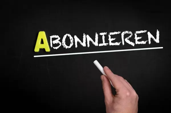 Hand schreibt “Abonnieren” auf schwarze Tafel