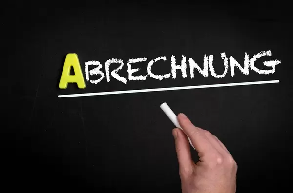 Hand schreibt “Abrechnung” auf schwarze Tafel