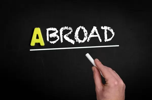 Hand schreibt “abroad” auf schwarze Tafel