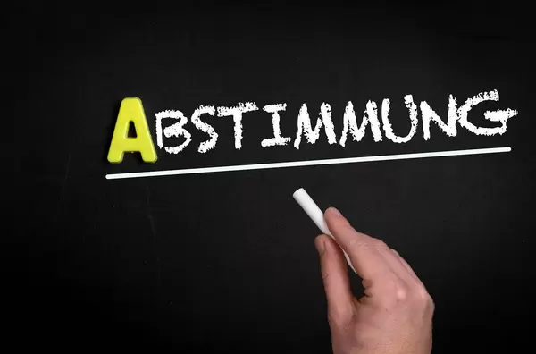 Hand schreibt “Abstimmung” auf schwarze Tafel