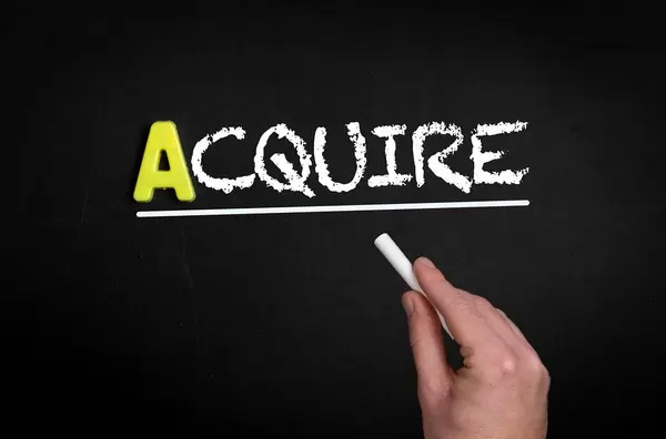 Hand schreibt “acquire” auf schwarze Tafel