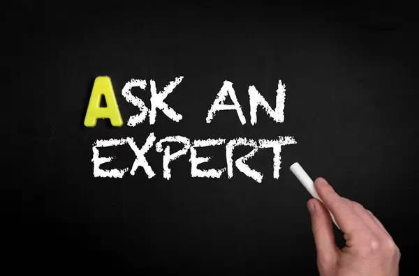 Hand schreibt  "Ask an expert" - Frage einen Experten - mit Kreide auf eine schwarze Tafel