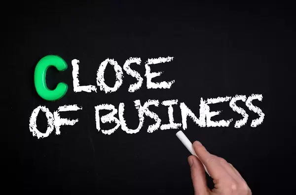 Hand schreibt "Close of Business" - Geschäftsschluss - mit Kreide auf eine schwarze Tafel