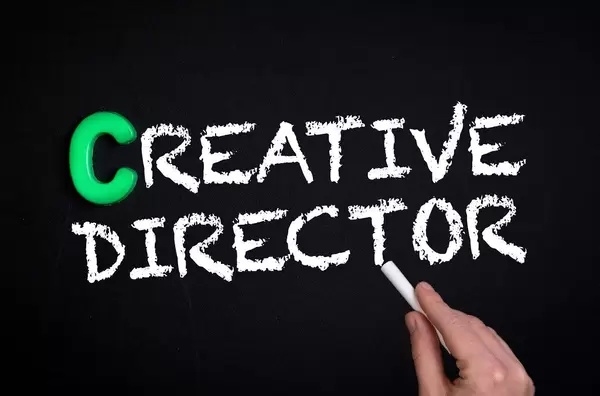Hand schreibt "Creative Director" mit Kreide auf eine schwarze Tafel