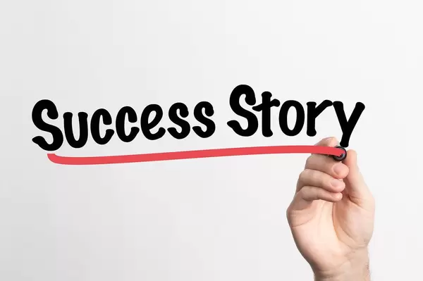 Hand schreibt "Erfolgsgeschichte" auf ein Whiteboard