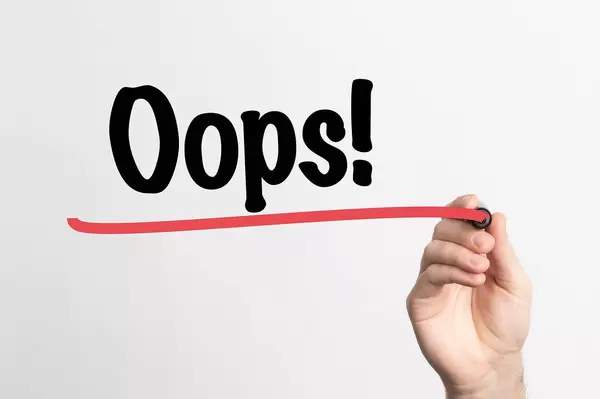 Hand schreibt "Oops! / Ups!" auf ein Whiteboard