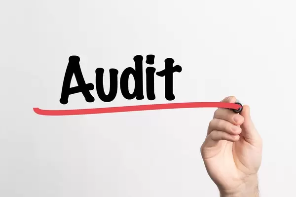 Hand schreibt "Überprüfung / Wirtschaftsprüfung / Audit" auf ein Whiteboard