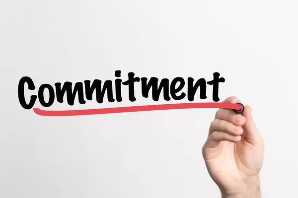 Hand schreibt "Verpflichtung / Engagement" auf ein Whiteboard