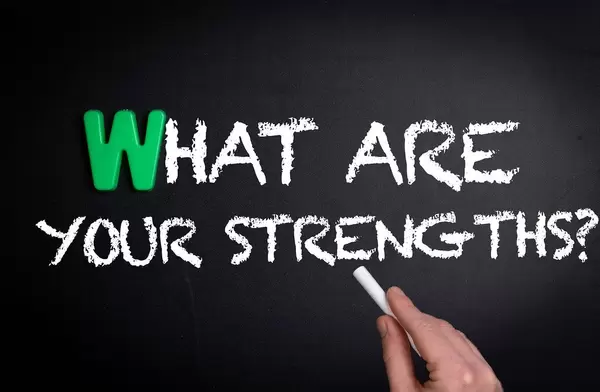 Hand schreibt "What are your strengths?" - was sind deine Stärken? - mit Kreide auf eine schwarze Tafel