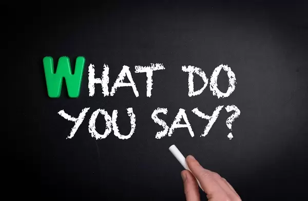 Hand schreibt "What do you say?" - Was sagst du? - mit Kreide auf eine schwarze Tafel