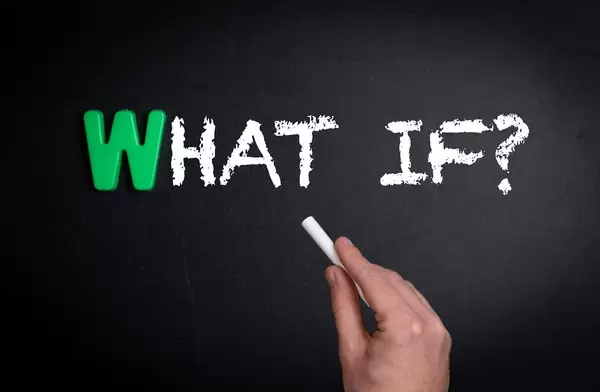 Hand schreibt "What if?" - Was wäre wenn - mit Kreide auf eine schwarze Tafel