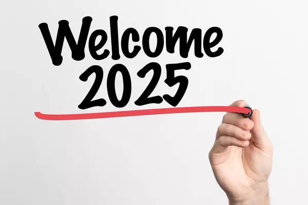 Hand schreibt "Willkommen 2025" auf ein Whiteboard