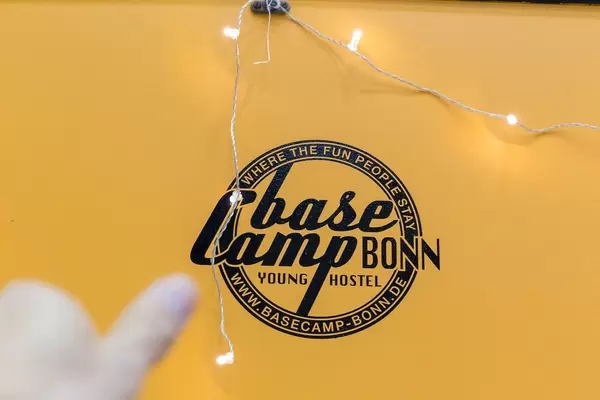 Hand shows to BaseCamp Bonn sign at the wall with the slogan "Where the fun people stay"